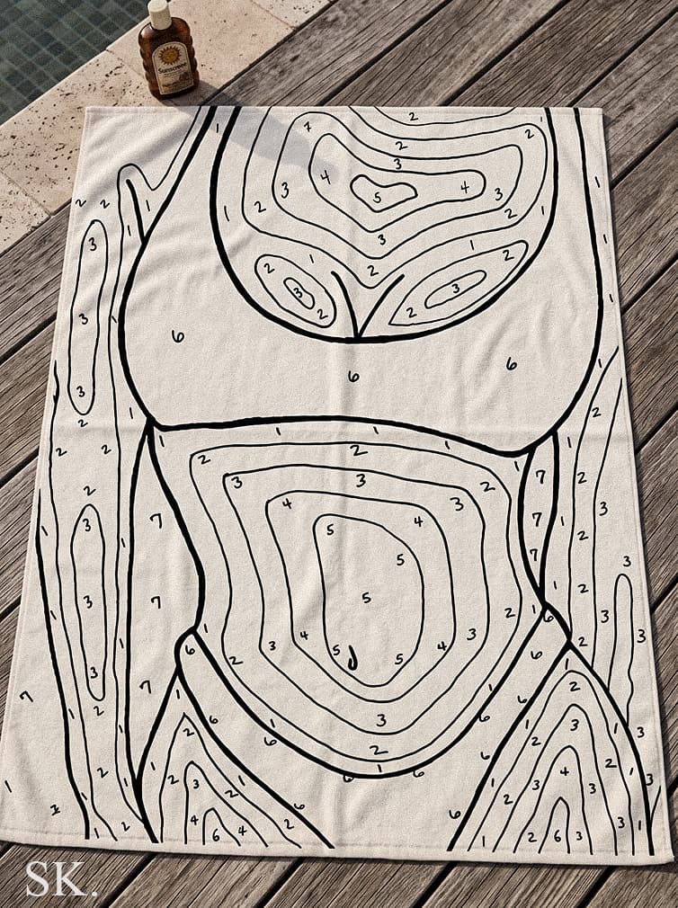 A white 'tan by numbers' beach towel with a black outline of a human body divided into numbered sections, resting on a wooden deck next to a pool with a bottle of sunscreen.