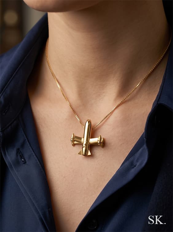 Close-up of a person wearing a polished gold airplane pendant on a delicate gold chain against a dark blue shirt.