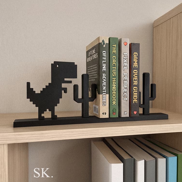 Black pixel art dinosaur and cactus bookends holding a stack of books on a wooden bookshelf, featuring retro gaming aesthetic.